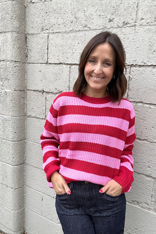Woman wearing a red and pink striped sweater against a gray brick wall.